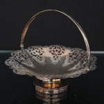 Fruteira em forma de cesta em metal prateado , corpo circular com borda recortada e decoração rendilhada de volutas, folhagens e elementos fitomórficos. Apoiada sobre base circular elevada e dotada de alça móvel arqueada. Apresenta desgaste do banho, oxidação superficial e marcas de uso compatíveis com o tempo. Medidas: Alt.: 14,5 x Diam.: 17,5 cm.