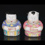 Duas(02) esculturas em porcelana oriental, modelados na forma de figuras infantis trajando vestes tradicionais, esmaltadas em policromia nas tonalidades azul, rosa, amarelo, verde e preto. As figuras apresentam inscrições em caracteres chineses na porção frontal e decoração floral distribuída pelas vestes. Medidas: Alt.: 8 x Comp.: 7 x Larg.: 5 cm.