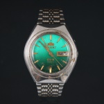 Relógio de pulso marca Orient, com caixa e pulseira em aço inoxidável. Mostrador em tonalidade verde com índices aplicados dourados, calendário duplo com indicação de dia da semana e data na posição de três horas, inscrição Automatic 21 Jewels e logotipo da manufatura. Fundo gravado Water Resistant, All Stainless Steel e referência UTA69-213-6B PR. Movimento mecânico automático de fabricação japonesa. Década de 1970/1980. Não está funcionando, apresenta desgastes e marcas de uso, vide foto.Medida: Diam.: 38 mm.