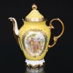 Bule em porcelana nacional, esmaltada em tom amarelo-claro, com tampa e perfil sinuoso, assente sobre pés recortados. Possui vertedor curvo e asa vazada de desenho inspirado no repertório rococó, ambos enriquecidos por aplicação de douração. Tampa de encaixe encimada por pomo facetado. A aba superior e a cobertura recebem friso rendilhado em ouro, complementado por filetes aplicados nas extremidades. Uma das faces exibe medalhão com composição pastoral, retratando casal em trajes de época acompanhado por mulher com criança em cenário ajardinado, circundado por moldura arabescada dourada. Base com marca de fábrica sob esmalte. Apresenta quebradura na borda. Medidas: Alt. 18 x Comp.: 16,5 x Larg.: 10 cm.