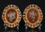 Par de placas decorativas de parede, de formato oval, com molduras em composição moldada e dourada, vazadas por volutas e elementos vegetalistas, contendo painéis centrais revestidos em veludo na tonalidade castanha, ornamentados por composição floral policroma. Trabalho decorativo de inspiração rococó. Medidas: Alt.: 19,5 x Comp.: 16,5 cm.