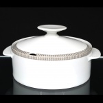 Porcelana Renner, Porto Alegre - RS(Fundada em 1937). Sopeira em porcelana nacional da década de 1960/70; esmaltação na cor branca, bordas ornadas por cercadura em meandro contínuo, de tonalidade cinza, e sucessão de quadrados duplos em douração aplicada, tampa ligeiramente abaulada encimada por puxador circular, alças laterais em abas integradas. Marca da manufatura no verso. Medidas: Alt.: 12,5 x Comp.: 15 x Larg.: 20,5 cm.