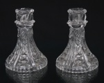 Par de castiçais em cristal moldado, com receptáculos circulares, colarinho decorado por motivo espiralado, corpo cônico ornamentado por reservas em leque e losangos facetados, terminando em base recortada. Medidas: Alt.: 13 x Diam.: 9,5 cm.