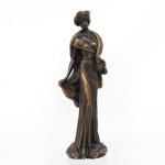 Escultura de dama em estilo Art Déco, executada em metal patinado com realces dourados, representando figura feminina trajando vestido longo, chapéu e estola, apoiada sobre base naturalista integrada. Medidas: Alt.:41 x Comp.: 13,5 x Larg.: 11 cm.