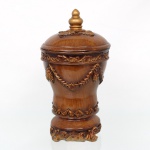 Pote decorativo com tampa, em madeira com realces dourados, corpo bojudo ornamentado por festões, pinhas e volutas em relevo, tampa abaulada encimada por pináculo torneado, base recortada com decoração rocaille. Marca Dimontti Italy Style. Medidas: Alt.: x Diam.: