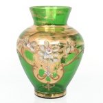 Vaso ornamental em vidro veneziano, tonalidade verde translúcido, corpo bojudo e colo alargado, decorado com faixa dourada aplicada e composição floral em esmalte policromado em relevo, com flores e folhagens estilizadas. Apresenta desgaste e perdas na douração. Medidas: Alt.: 20 x Diam.: 15 cm.