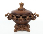 Bombonière com tampa, executada em resina moldada com acabamento simulando madeira patinada e realces dourados. Corpo circular com galeria vazada decorada por motivos de concheados e volutas, apresentando alças laterais recortadas. Tampa abaulada encimada por pega em forma de botão floral. Base elevada com decoração de inspiração rococó, composta por elementos de acanto, conchas e frisos perolados. Medidas: Alt.: 18 x Comp.: 22 x Larg.: 16 cm.