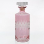 Garrafa licoreira em cristal rosado, corpo cilíndrico com decoração lapidada em faixa de motivos losangulares foscos, gargalo curto e tampa facetada em cristal incolor. Medidas: Alt.: 25,5 x Diam.: 10 cm.