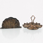 Dois(02) itens em metal prateado: Um(01) porta-guardanapos com decoração em relevo de motivo radial, e uma petisqueira vazada e cinzelada, formada por quatro compartimentos lobulados com alça central recortada. Necessita refazer banho de prata. Medidas petisqueira: Alt.: 9 x Diam.: 14 cm. Medidas porta-guardanapo: Alt.: 7 x Comp.: 14 cm.