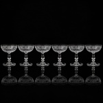 Belíssimo conjunto de taças francesas em cristal, do início do século XX, para serviço de champanhe; bojo hemisférico gravado com medalhão ovalado com composição simétrica formado por grinaldas suspensas, laçarias, festões e cartelas radiadas, circundada por friso perlado e motivos fitmorfos, borda com cercadura composta por enrolamento vegetalistas, palmetas estilizadas, volutas e elementos foliáceos repetidos em sequência linear; fuste balaústre, contendo anel intermediário, sobre base circular. Composto de seis(06) unidades. Medidas: Alt.: 10,5 x Diam.: 10 cm.