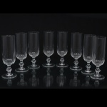 Conjunto de oito(08) flutes em cristal incolor moldado, com bojo cilíndrico alongado, decoração em gomos verticais na porção inferior, haste facetada com nó central e pé circular. Medidas: Alt.: 16 x Diam.: 5 cm.