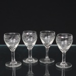 Quatro(04) taças para licor em meio cristal, diáfano e incolor, bojo oval talhado com frutos e folhagens, fuste tubular sobre base circular. Medidas: Alt.: 8 x Diam.: 4 cm.