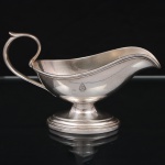 Art Krupp Metal, Bendorf - Alemanha(Fundada por Friedrich Krupp em 1811). Molheira em metal prateado, corpo de perfil naviforme, assente sobre pé oval escalonado, provida de asa vazada em voluta e bico vertedor recurvado. Apresenta brasão marcada no bojo com monograma "H.A.P.A.G." encimado por âncora, pertencente à Hamburg-Amerikanische Packetfahrt-Actien-Gesellschaft, companhia de navegação alemã. Marca da manufatura ao fundo. Possui marcas de uso. Medidas: Alt.: 10 x Comp.: 16 x Larg.: 7 cm.