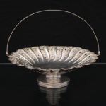 AUREA PRATA 90. Centro de mesa em metal prateado, de formato circular e interior côncavo, assente sobre base alteada. Corpo moldado em gomos verticais, com borda ondulada e decoração vazada e gravada em padrão floral estilizado, composta por flores e folhagens sinuosas de inspiração Art Nouveau. Dotado de alça móvel arqueada. Executado em chapa estampada, cinzelada e recortada. Apresenta sinais de uso. Marca da manufatura no verso. Medidas: Alt.: 19,5 x Diam.: 23,5 cm.