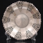 AUREA PRATA 90. Pequena fruteira confeccionada em metal prateado, formato hemisférico raso, borda recortada, decorado por reservas vazadas em composição simétrica de motivo vegetalista, com entrelaçados, volutas e estilizações florais, executado em chapa estampada, recortada, vazada e gravada. Marca da manufatura no verso. Apresenta marcas de uso. Medidas: Alt.: 2,5 x Diam.: 15,5 cm.