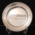 FRACALANZA. Elegante bandeja confeccionada em metal espessurado à prata, formato circular, centro ligeiramente rebaixado, borda relevada com fileira de frisos intercaladas por fitas cruzadas, ornato obtido através da técnica do cinzelado. Marca da manufatura no verso. Apresenta marcas de uso. Medida: Diam.:  cm.