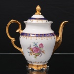 Porcelana Schmidt - Brasil(Fundada em 1945). Exuberante bule para café em porcelana nacional da década de 1950/60, executado ao estilo francês do período Luís XV; esmaltagem vítrea na cor branca, faixas de tonalidade azul cobalto, profusamente realçada com frisos, faixa com repetição de motivos fitomorfos em padrão seriado; reservas florais compostas por rosas, violetas e pequenas flores campestres, distribuídas no bojo; bico curvilíneo de ponta recortada, asa lateral em grande voluta, tampa campaniforme encimada por puxador modelado em forma de fruto sobre laçarote, base circular recortada. Marca da manufatura ao fundo. Medidas: Alt.: 23 x Comp.: 22,5 x Larg.: 13 cm.