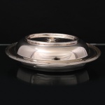 FRACALANZA. Elegante terrina com tampa confeccionada em metal espessurado à prata, paraserviço de  vegetai; formato oval de centro rebaixado, borda ornamentada com fileira de frisos relevados, intercalado por fitas, padrão império francês, obtidos através da técnica do cinzelado, ornato replicado na tampa. Originalmente com puxador removível(perdido neste exemplpar), tornando a tampa um segunda travessa. Marca da manufatura no verso. Med.: Alt. 7 x Comp. 27 x Larg. 21 cm. Apresenta marcas de uso.