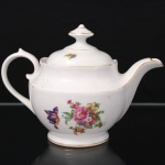 Porcelana Real, Mauá - SP(Fundada em 1943 por Fritz Erwin Schmidt). Bule para chá em porcelana nacional da década de 1950/60; esmaltação branca, decorada com padrão floral em estampagem policromada, distribuídas no bojo em arranjos, e na tampa com flores soltas; contornos realçados por filete em douradura; bojo hemisférico sobre base circular, borda revirada para fora e recortada em arcos, tampa abaulada encimada por puxador com feitio de pião, bico vertedor curto e curvado, alça lateral em voluta. Marca da manufatura ao fundo. Medidas: Alt.: 15 x Comp.: 21,5 x Larg.: 13 cm. Apresenta um ínfimo bicado na borda da boca.
