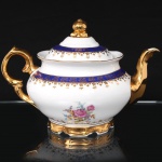 Porcelana Schmidt - Brasil(Fundada em 1945). Exuberante bule para chá em porcelana nacional da década de 1950/60, executado ao estilo francês do período Luís XV; esmaltagem vítrea na cor branca, faixas de tonalidade azul cobalto, profusamente realçada com frisos, faixa com repetição de motivos fitomorfos em padrão seriado; reservas florais compostas por rosas, violetas e pequenas flores campestres, distribuídas no bojo; bico curvilíneo de ponta recortada, asa lateral em grande voluta, tampa campaniforme encimada por puxador modelado em forma de fruto sobre laçarote, base circular recortada. Marca da manufatura ao fundo. Medidas: Alt.: 16 x Comp.: 23,5 x Larg.: 15,5 cm.
