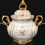 Porcelana Real, Mauá - SP (fundada em 1943 por Fritz Erwin Schmidt). Açucareiro com tampa em porcelana nacional, década de 1960/70, corpo moldado em gomos, acabamento nacarado e decoração em douração aplicada à mão com motivos vegetalistas. Alças laterais vazadas de desenho rocaille, tampa encaixada com pega vazada e base moldada. Marca da manufatura ao fundo. Apresenta fio de cabelo. Medidas: Alt.: x Comp.: x Larg.:
