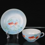 Xícara para chá com respectivo pires em porcelana japonesa, decoração policroma representando peixe ornamental em tonalidades laranja sobre fundo azul degradê, com elementos vegetalistas estilizados. Marca da manufatura japonesa na face inferior, composta por escudo com monograma N sob sol nascente, acompanhada de caracteres japoneses.  Medidas: Xícara: Alt.: x Comp.: x Larg.: ; Pires: Diam.:
