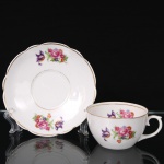 Porcelana Real, Mauá - SP(Fundada em 1943 por Fritz Erwin Schmidt). Xícara para chá em porcelana nacional da década de 1950/60; esmaltação branca, bojo hemisférico e alça lateral em voluta, decorada com padrão floral em estampagem policromada, contornos realçados por filete em douradura; pires com borda recortada em arcos. Marca da manufatura ao fundo. Medidas: Xícara: Alt.: 5 x Comp.: 10,5 x Larg.: 8,5 cm; Medidas: Pires: Diam.: 14,5 cm.