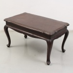 Mesa de centro em madeira nobre estilo Luís XV. Tampo retangular de contorno recortado e movimentado, com moldura escalonada acompanhando o desenho perimetral. Caixa lisa com saia recortada e quatro pernas cabriolé terminadas em pés enrolados. Apresenta desgastes no acabamento, riscos, marcas de uso e perdas pontuais compatíveis com a utilização e o tempo. Medidas: Alt.: x Comp.: x Larg.:
