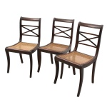 Conjunto de três cadeiras em madeira nobre e palhinha natural. Espaldares vazados com travessa superior arqueada e elemento central em X com roseta torneada ao centro. Assentos em palhinha sextavada encaixada em moldura lisa. Estrutura com montantes e pernas dianteiras ligeiramente sabreadas, terminadas em pés retos. Trabalho de inspiração neoclássica, executado no século XX, destinado a sala de jantar. Apresentam desgastes no acabamento, riscos, marcas de uso, pequenas perdas e manchas pontuais, compatíveis com a utilização e o tempo. Medidas: Alt.: 88 x Comp.: 45 x Larg.: 42 cm.
