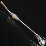 Antiga bomba para chimarrão confeccionada em metal prateado, passador e boquilha decorados com douradura. Med.: Comp. 19 cm.