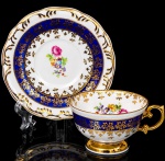 Porcelana Schmidt - Brasil(Fundada em 1945). Exuberante xícara para café em porcelana nacional da década de 1950/60, executado ao estilo francês do período Luís XV; esmaltagem vítrea na cor branca, faixas de tonalidade azul cobalto, profusamente realçada com frisos, faixa com repetição de motivos fitomorfos em padrão seriado; reservas florais compostas por rosas, violetas e pequenas flores campestres, distribuídas ao centro do pires, bem como no interior da xícara complementam a composição, bojo hemisférico assente sobre base alteada, asa lateral em voluta. Marca da manufatura ao fundo. Medidas: Chávena: Alt.: 4,5 x Comp.: 8,5 x Larg.: 7 cm; Pires: Diam.: 11 cm.