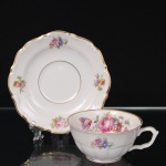 C.T. Tielsch, Walbrzych (antiga Altwasser) - Polônia. Belísima xícara para chá em porcelana polonesa da década de 1390/40; esmaltagem vítrea na cor branca, decorada em policromia com composição floral constituídas por rosas, tulipas e flores campestres, distribuídas em reservas no interior da xícara, no bojo e no pires, aplicada em estampagem; bordas realçadas por filetes dourados. Marca da manufatura no verso. Medidas: Xícara: Alt.: 5 x Comp: 12 x Larg.: 9,5 cm. ; Pires: Diam.: 15 cm.
