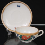 Xícara para chá em porcelana oriental, dito casca de ovo", esmaltação branca, bojo hemisférico sobre base circular, alça lateral em voluta; corpo esmaltado com decoração policroma de flores estilizadas em vermelho, azul e verde, acompanhadas de borboletas, borda circundada por faixa em tom ocre e filete preto. Medidas: Xícara: Alt.: 4 x Comp.: 10,5 x Larg.: 8,5 cm; Pires: Diam.: 13 cm.