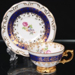 Porcelana Schmidt - Brasil(Fundada em 1945). Exuberante xícara para café em porcelana nacional da década de 1950/60, executado ao estilo francês do período Luís XV; esmaltagem vítrea na cor branca, faixas de tonalidade azul cobalto, profusamente realçada com frisos, faixa com repetição de motivos fitomorfos em padrão seriado; reservas florais compostas por rosas, violetas e pequenas flores campestres, distribuídas ao centro do pires, bem como no interior da xícara complementam a composição, bojo hemisférico assente sobre base alteada, asa lateral em voluta. Marca da manufatura ao fundo. Medidas: Chávena: Alt.: 4,5 x Comp.: 8,5 x Larg.: 7 cm; Pires: Diam.: 11 cm.