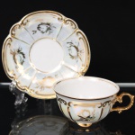 Porcelana Real, Mauá - SP(Fundada em 1943 por Fritz Erwin Schmidt). Xícara para café em porcelana nacional da década de 1960/70; bojo hemisférico moldado com gomos, decorado em douração aplicada à mão com motivos vegetalistas e volutas estilizadas, apresentando acabamento nacarado, asa lateral vazada de desenho rocaille e pires recortado em contorno ondulado. Marca da manufatura no verso. Medidas: Xícara: Alt.: 4 x Comp.: 9 x Larg.: 7 cm. ; Pires: Diam.: 10,5 cm.