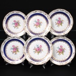 Porcelana Schmidt - Brasil(Fundada em 1945). Exuberante conjunto de pratos para sobremesa em porcelana nacional da década de 1950/60, executado ao estilo francês do período Luís XV; esmaltagem vítrea na cor branca, circundada por faixa de tonalidade azul cobalto, profusamente realçada com frisos e faixa com repetição de motivos fitomorfos em douradura; reserva floral compostas por rosas, violetas e pequenas flores campestres ao centro, orla relevada com aplicações em relevo ao longo da aba. Marca da manufatura ao fundo. Composto de seis(06) unidades. Medidas: Diam.: 18,5 cm.