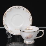 Porcelana Schmidt - Brasil(Fundada em 1945). Xícara para chá em porcelana nacional, esmaltação branca, decoração floral policromada com detalhes dourados. Bojo hemisférico assentado sobre pé anelar destacado, bordas recortadas e contornadas por filetes em ouro. Apresenta inscrição comemorativa em dourado 80 anos Aldenir no interior da xícara. Marca da manufatura no verso. Medidas: Xícara: Alt.: 5 x Comp.: 8,5 x Larg.: 7 cm. ; Pires: Diam.: 11 cm.