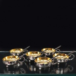 Conjunto de taças para sobremesa confeccionado em metal espessurado à prata, bojo hemisférico raso, apoiado sobre três pés esféricos, alça lateral em voluta. Composto de seis(06) unidades. Medidas: Taça: Alt.: 3,5 x Comp.: 11 x Larg.: 8,5 cm. ; Colher: Comp.: 12,5 cm.