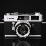 Câmera fotográfica Canon Canonet QL, corpo metálico com revestimento em material sintético texturizado na cor preta, equipada com objetiva fixa Canon Lens SE 45 mm f/1.9. Modelo telemétrico de visor direto, dotado do sistema Quick Load (QL) para carregamento rápido de filme 35 mm, produzido no Japão na década de 1960. Apresenta sapata para flash, comandos mecânicos de exposição e olhais laterais para fixação de alça de transporte. Inscrições do fabricante e numeração de série no corpo. Não testado, sem garantias de funcionamento. Medidas: Alt.: 9 x Comp.: 14 x Larg.: 7 cm.