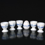 Porcelana, Steatita e Magnésia S/A, Campo Largo - PR(Fundada em 1954). Conjunto para serviço de ovos em porcelana, composto por cinco(05) porta-ovos e um(01) saleiro de mesa, decorados em esmalte azul com composição floral e cercaduras lineares. Porta-ovos com bojo oval sobre pé circular; saleiro de formato ovóide perfurado. Marca da manufatura ao fundo. Medidas saleiro: Alt.: 6 x Diam.: 5 cm. ; Medidas porta-ovo: Alt.:6 x Diam.: 5 cm.