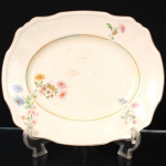 Alfred Meakin, Staffordshire - Inglaterra(Fundada em 1875, ativa até 1976). Travessa da década de 1930 em faiança inglesa, estilo e período Art Déco; esmaltagem de tom marfim, decorada com o padrão "Marigold", borda recortada e aba moldada, decorada com composição floral policromada e filetes em tonalidades verde e dourada. Marca da manufatura no verso. Medidas: Comp.: x Larg.: