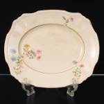 Alfred Meakin, Staffordshire - Inglaterra(Fundada em 1875, ativa até 1976). Travessa da década de 1930 em faiança inglesa, estilo e período Art Déco; esmaltagem de tom marfim, decorada com o padrão "Marigold", borda recortada e aba moldada, decorada com composição floral policromada e filetes em tonalidades verde e dourada. Marca da manufatura no verso. Medidas: Comp.: 32 x Larg.: 27 cm.