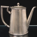 FRACALANZA. Cafeteira em metal prateado, destinada ao serviço de café, corpo cônico, bico vertedor tubular, tampa articulada com pega torneada e alça geométrica. Marca da manufatura ao fundo. Medidas: Alt.: x Comp.: x Larg.: .Apresenta degastes do banho de prata.