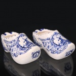 Par de pequenos tamancos decorativos em faiança, manufatura holandesa, formato tradicional neerlandês, com decoração em azul sob esmalte representando moinho, paisagem rural, elementos florais e ornatos. Marcados na base Handmade Holland Delft Blue. Medidas: Alt.: x Comp.: x Larg.: