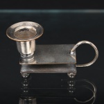 EBERLE. Palmatória com fosforeira confeccionada em metal espessurado à prata, arandela cilíndrica de borda revirada, alça lateral curvada, assente sobre três pés esféricos. Marca da manufatura puncionada no verso. Alt. 5,5 x Comp. 10 x Larg. 4 cm.