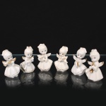 Conjunto de seis(06) estatuetas de anjos musicistas em porcelana, com realces dourados aplicados nos instrumentos e detalhes do vestuário, representadas em trajes longos estilizados, portando diferentes instrumentos musicais, incluindo flauta, alaúde, harpa, partitura, címbalo e trombeta. Medidas: Alt.: 6,5 x Comp.: 4 x Larg.: 2 cm.
