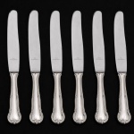 MERIDIONAL EPNS(100). Elegante conjunto de facas médias confeccionadas em metal espessurado à prata, lâminas em aço inox. Cabo de ponta arredondada, borda contornada com volutas relevadas, obtidas através da técnica do cinzelado. Marca da manufatura no verso do cabo. Composto de cinco(05) unidades. Medida: Comp.: 20,5 cm.
