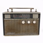 Rádio portátil de 8 transistores, executado em caixa revestida em material sintético texturizado, com grade frontal metálica, alça superior rígida, antena retrátil e mostrador horizontal policromado com indicação para ondas médias, tropicais e curtas. Comandos frontais circulares para sintonia, volume e seleção de faixas. Produção brasileira, circa 19601970. Não foi testado, sem garantias de funcionamento. Apresenta desgastes, marcas de uso e do tempo. Medidas: Alt.: 26 x Comp.: 33 x Larg.: 13 cm.