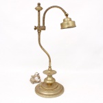 Luminária de mesa articulada em metal dourado, com haste sinuosa e braço móvel terminado em cúpula cilíndrica direcionável, montada sobre base circular escalonada. Estrutura com elementos torneados e sistema de regulagem lateral por parafuso de aperto. Apresenta sinais de oxidação e marcas de uso, parte elétrica não testada. Medidas: Alt.: 56 x Comp.: 24 x Larg.: 19 cm.