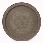 Grande bandeja circular em latão patinado, cinzelado e gravado, decoração orientalista composta por caractere chinês Fu (fortuna) ao centro, cercado por reservas figurativas alusivas ao zodíaco chinês, com representações de dragão, ave, coelho e motivos florais, intercalados por faixas geométricas e borda recortada. Possui alça no verso para fixação em parede. Medida: Diam.: 90 cm.